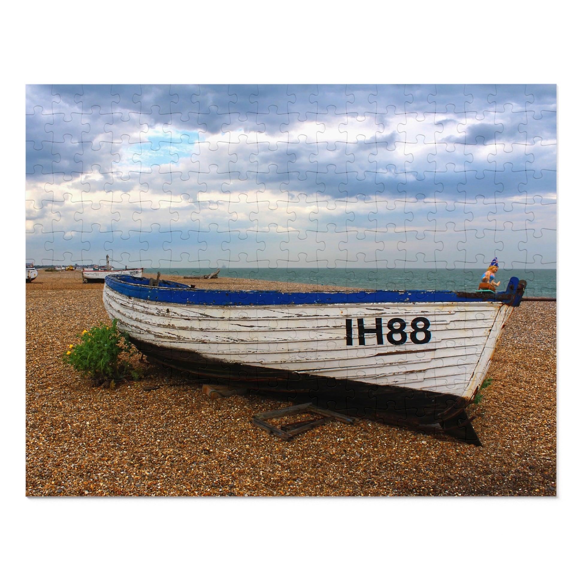 White boat with blue trim on a pebbly beach under a cloudy sky.