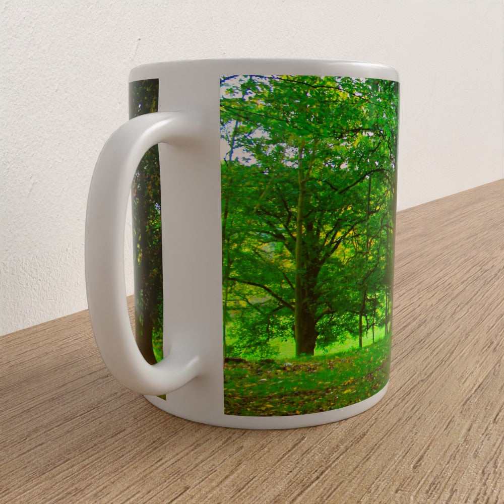 White mug with a scenic design of trees and greenery on a wooden surface.