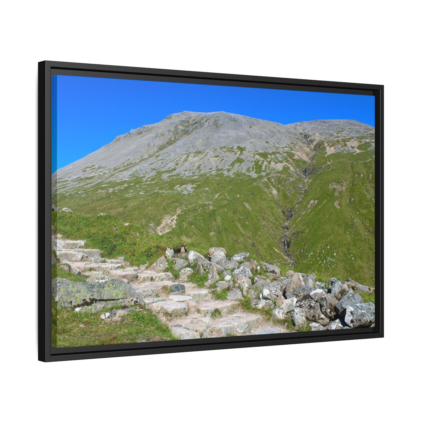 Framed picture of a mountain landscape with greenery and clear blue sky.