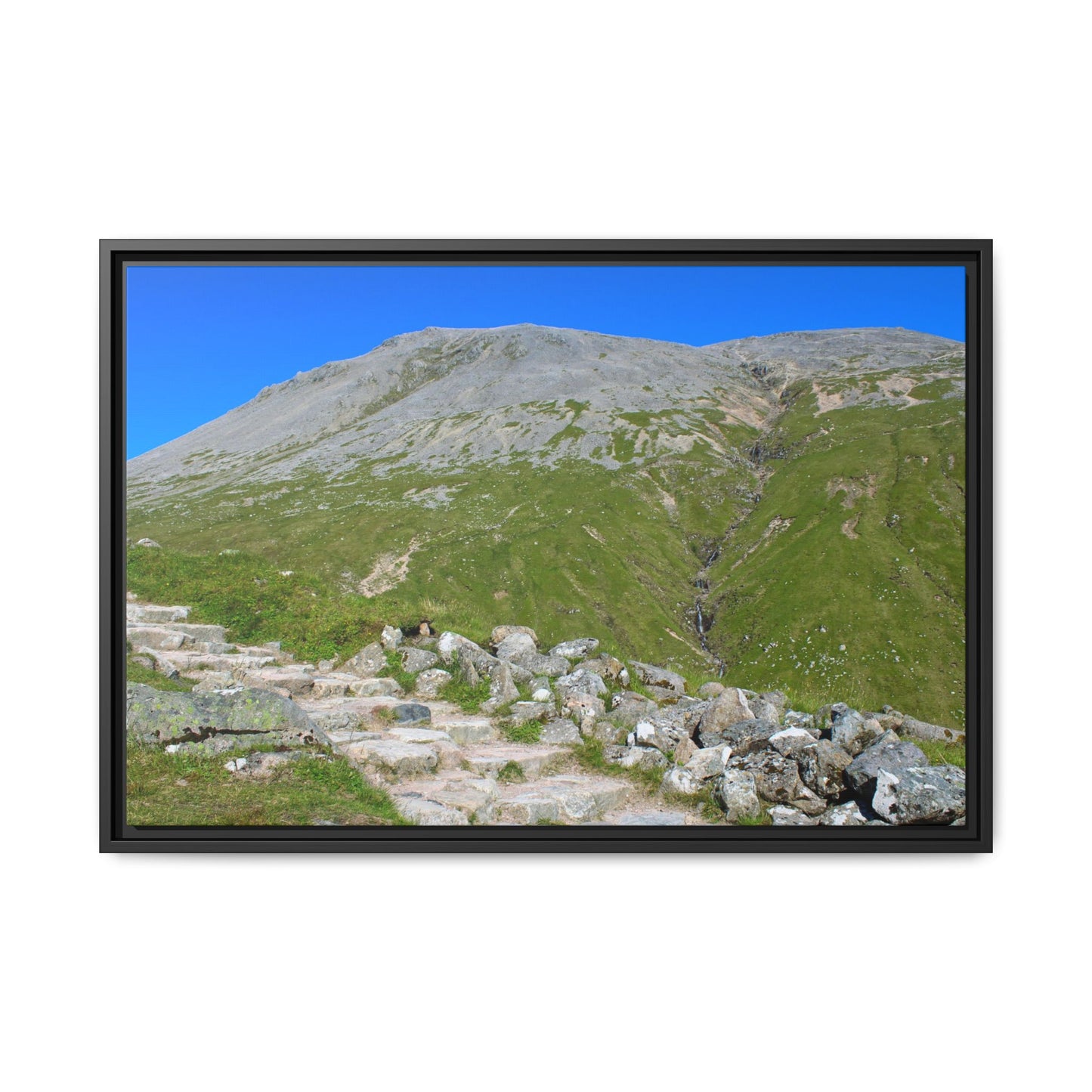 Framed photograph of a mountain landscape with green slopes and clear blue sky.
