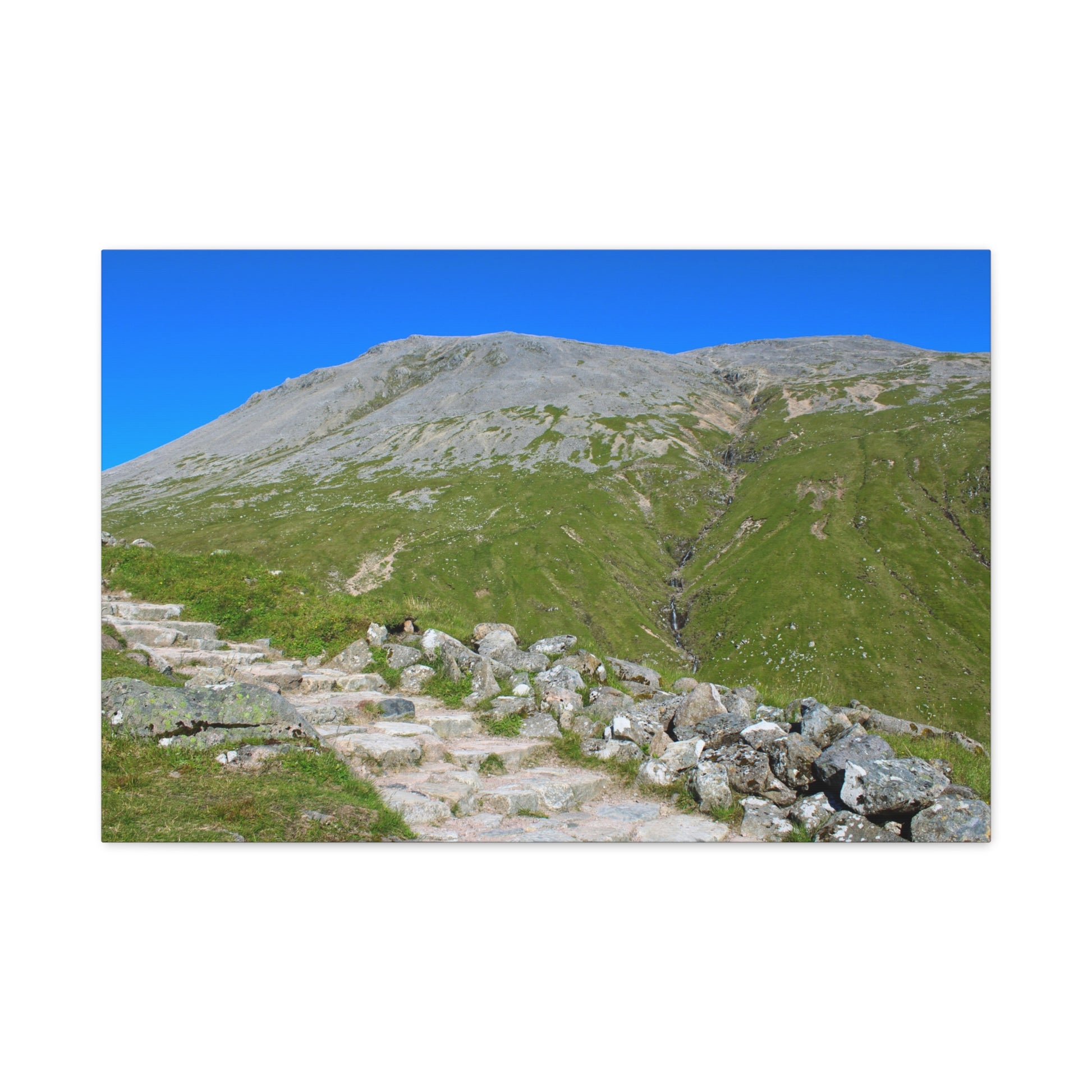 Mountain landscape with rocky foreground and grassy slopes under a clear blue sky