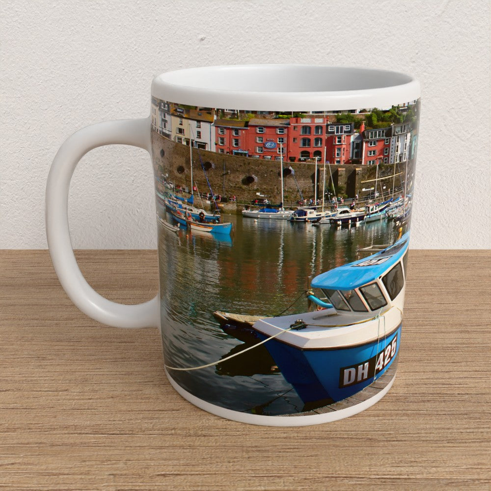 Mug with a scenic design of boats and buildings on a wooden surface