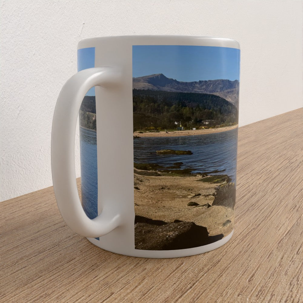 Mug with a scenic design of a lake and mountains on a wooden surface.