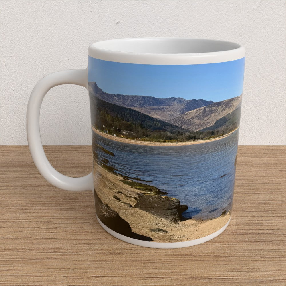 Mug with a scenic design of mountains and water on a wooden surface