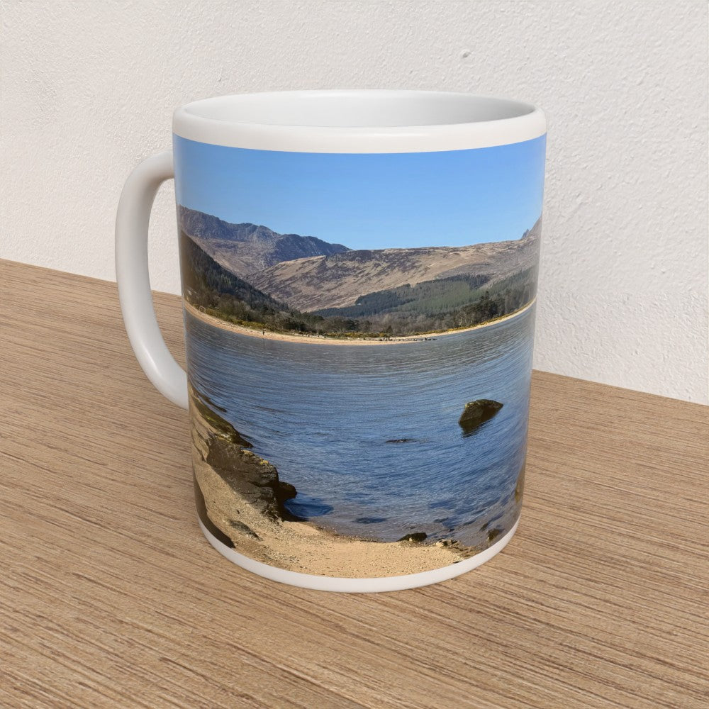Mug with a scenic design of mountains and water on a wooden surface