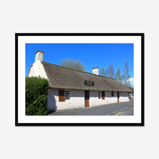 Framed picture of a thatched cottage with a clear blue sky.