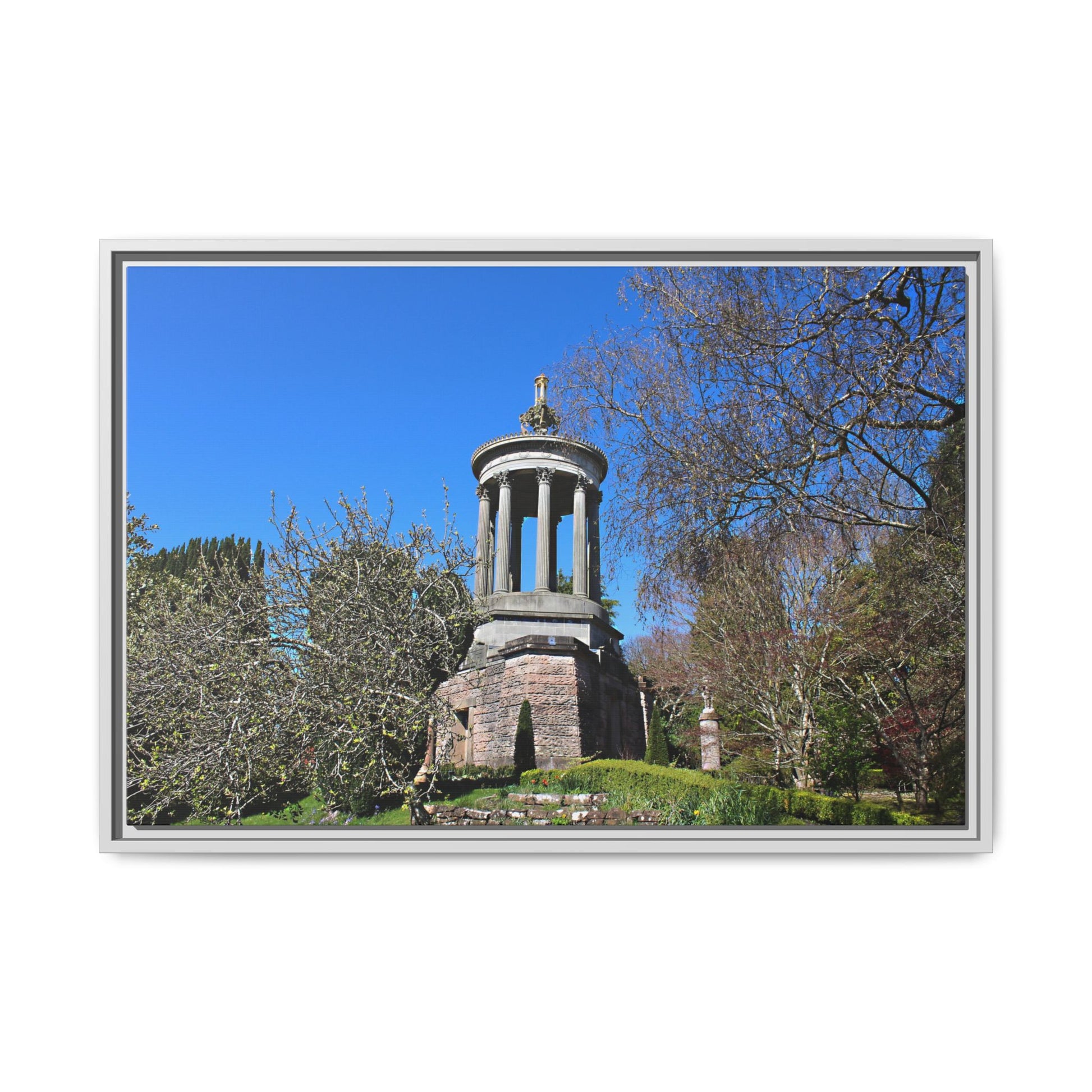 Stone monument with a statue in a park setting under a clear blue sky.