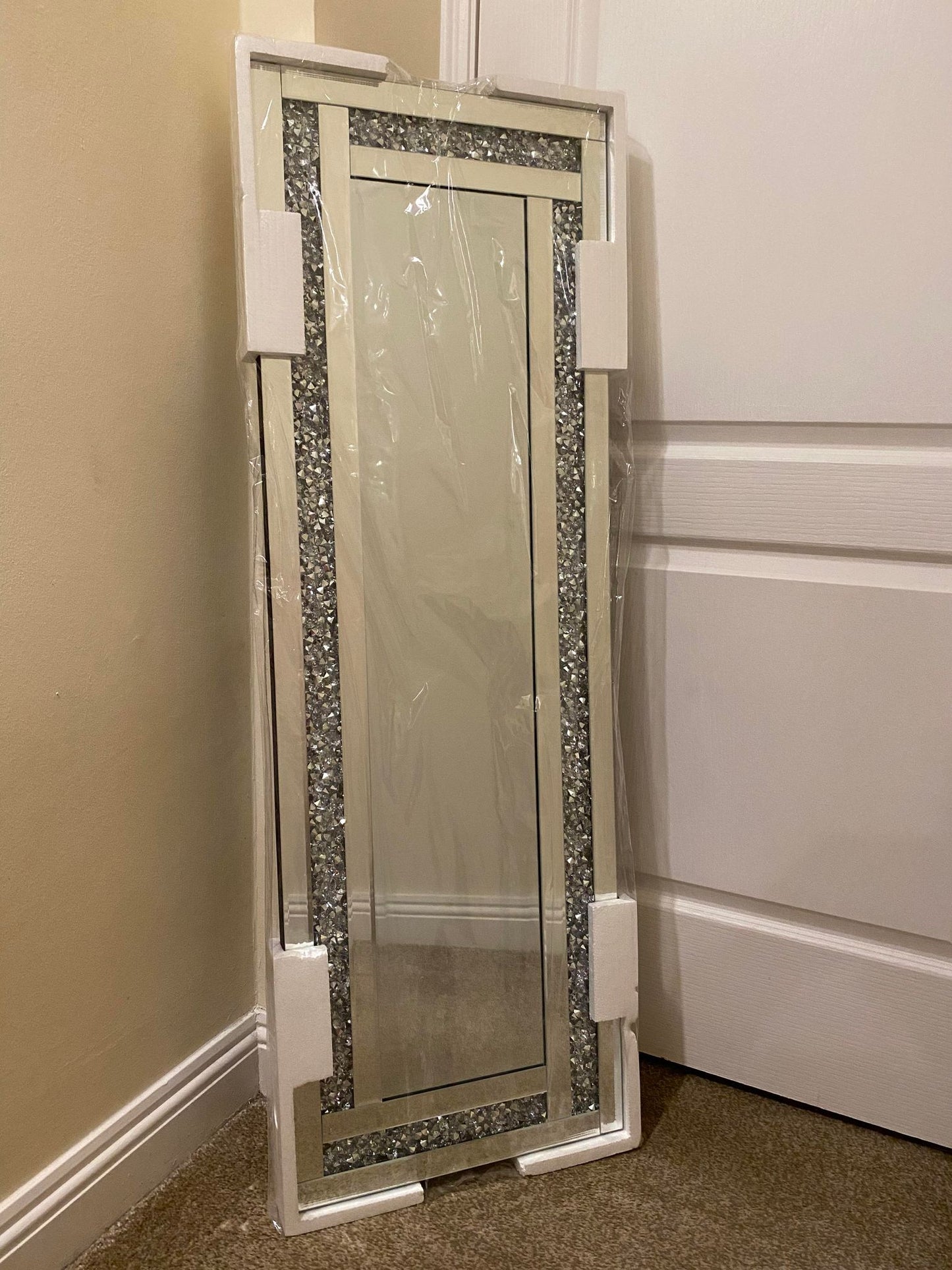 A silver bevelled edge mirror with crushed crystal detailing, standing upright against a wall.
