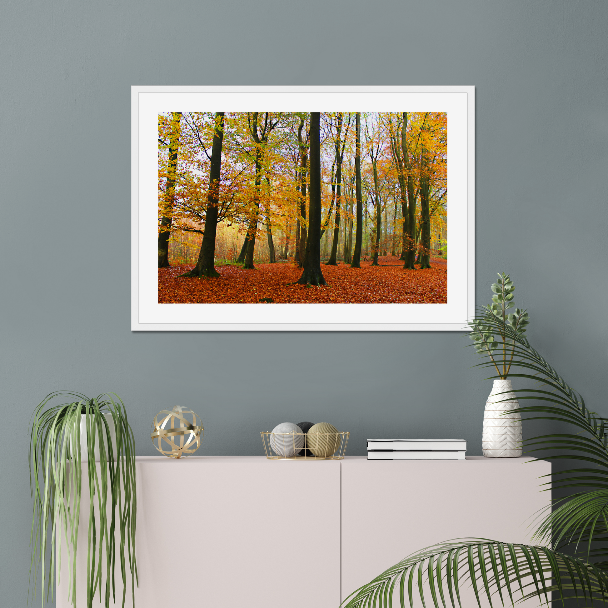 Framed print of a forest scene with autumn colors on a gray wall above a white cabinet.