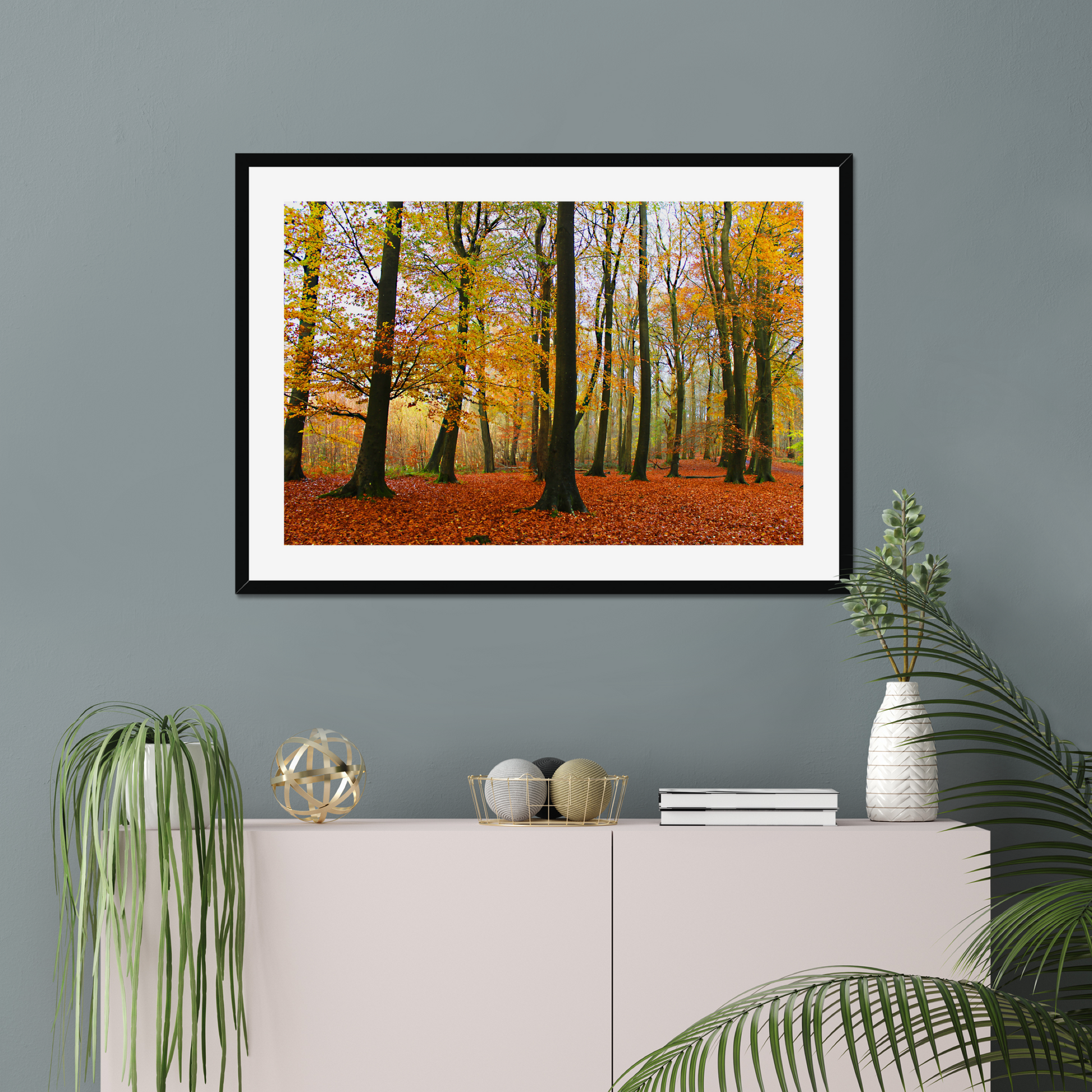 Framed print of a forest scene with autumn colors on a gray wall above a white cabinet.