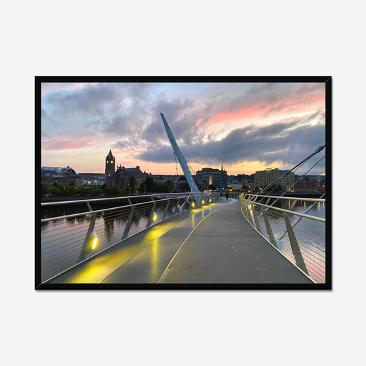 Framed photograph of a modern bridge with a cityscape and sunset in the background.
