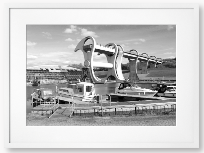 Black and White framed photo of the Falkirk Wheel boat lift with boats docked at a marina under a clear sky.