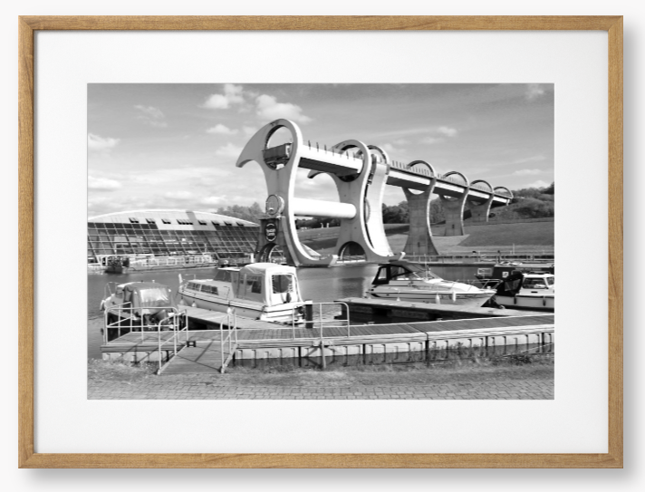 Black and White framed photo of the Falkirk Wheel boat lift with boats docked at a marina under a clear sky.