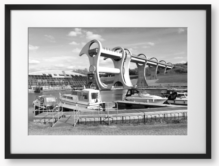 Black and White framed photo of the Falkirk Wheel boat lift with boats docked at a marina under a clear sky.