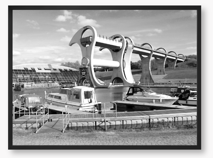 Black and White framed photo of the Falkirk Wheel boat lift with boats docked at a marina under a clear sky.