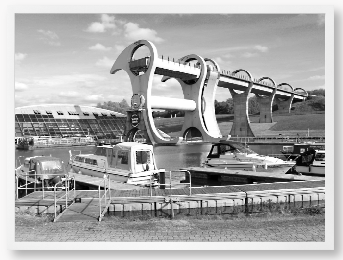 Black and White framed photo of the Falkirk Wheel boat lift with boats docked at a marina under a clear sky.