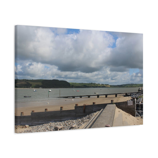 Panoramic view of a coastal scene with a bridge, water, and hills under a cloudy sky.