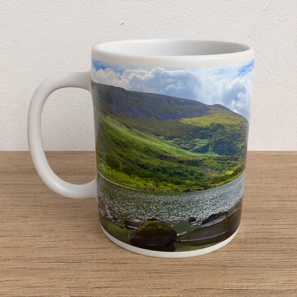 Mug with a scenic design of a lake and mountains on a wooden surface.