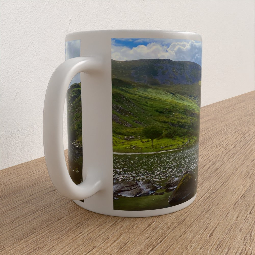 White mug with a scenic landscape of mountains and fields on a wooden surface.