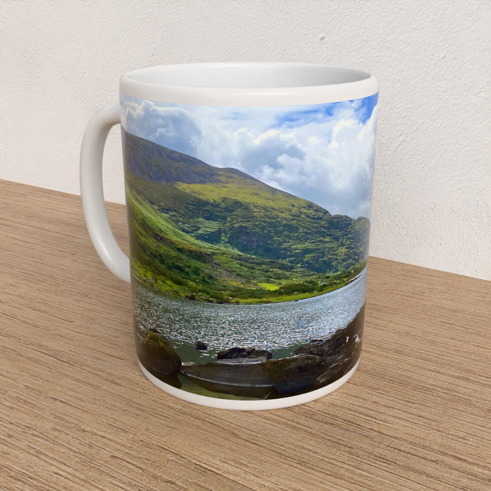 Mug with a scenic design of a lake and mountains on a wooden surface.
