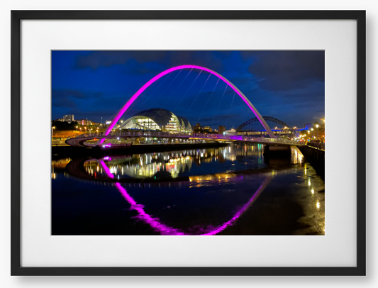 Framed photo of a modern bridge with a purple arch over water at night.