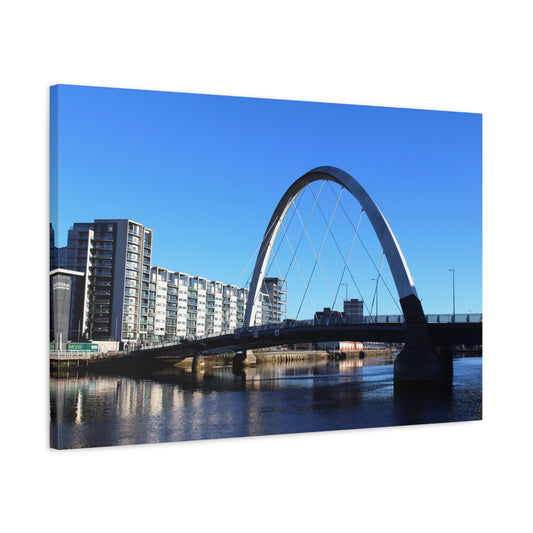 Modern arch bridge over a body of water with buildings in the background