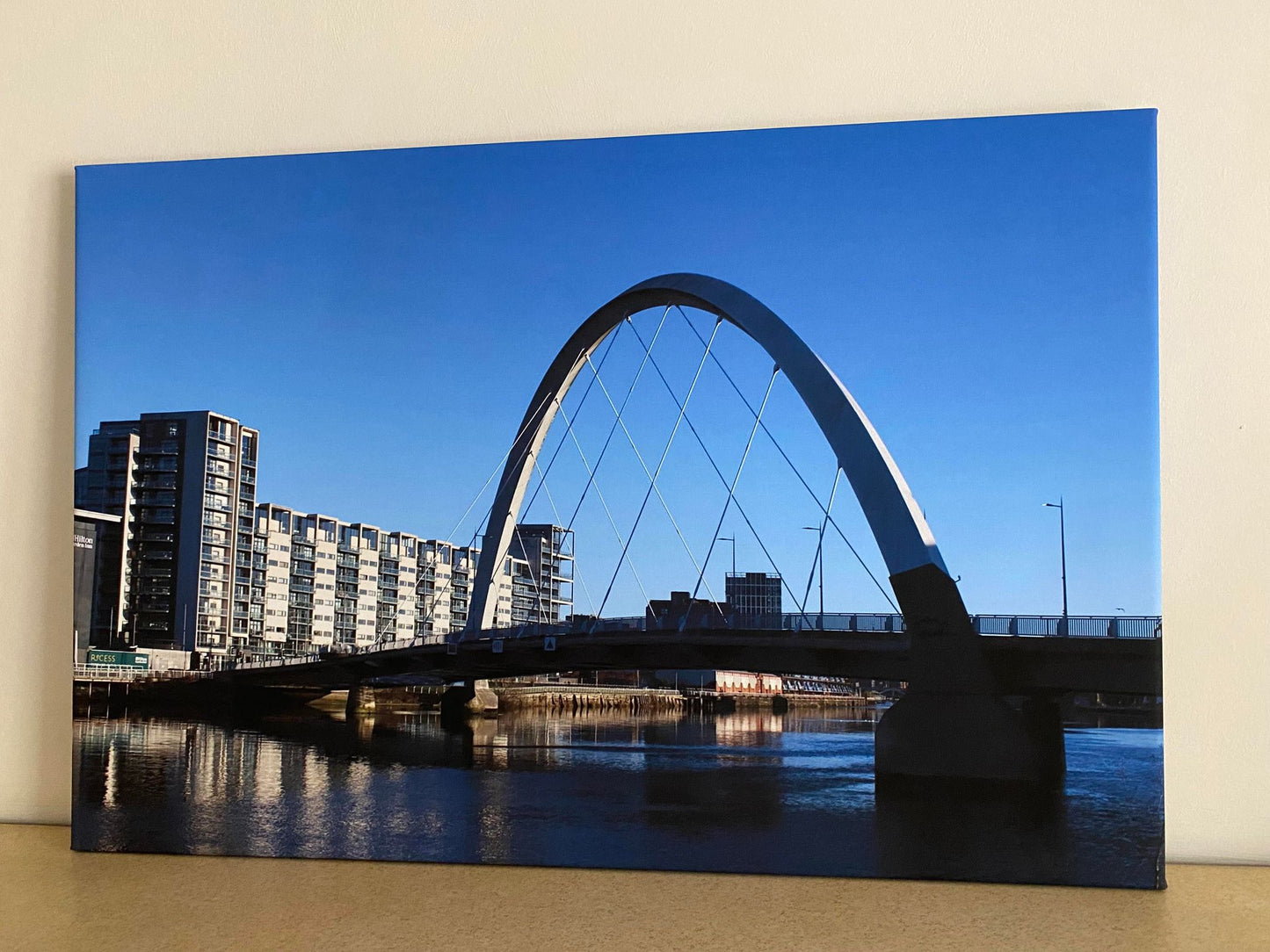 Suspended arch bridge over water with buildings in the background
