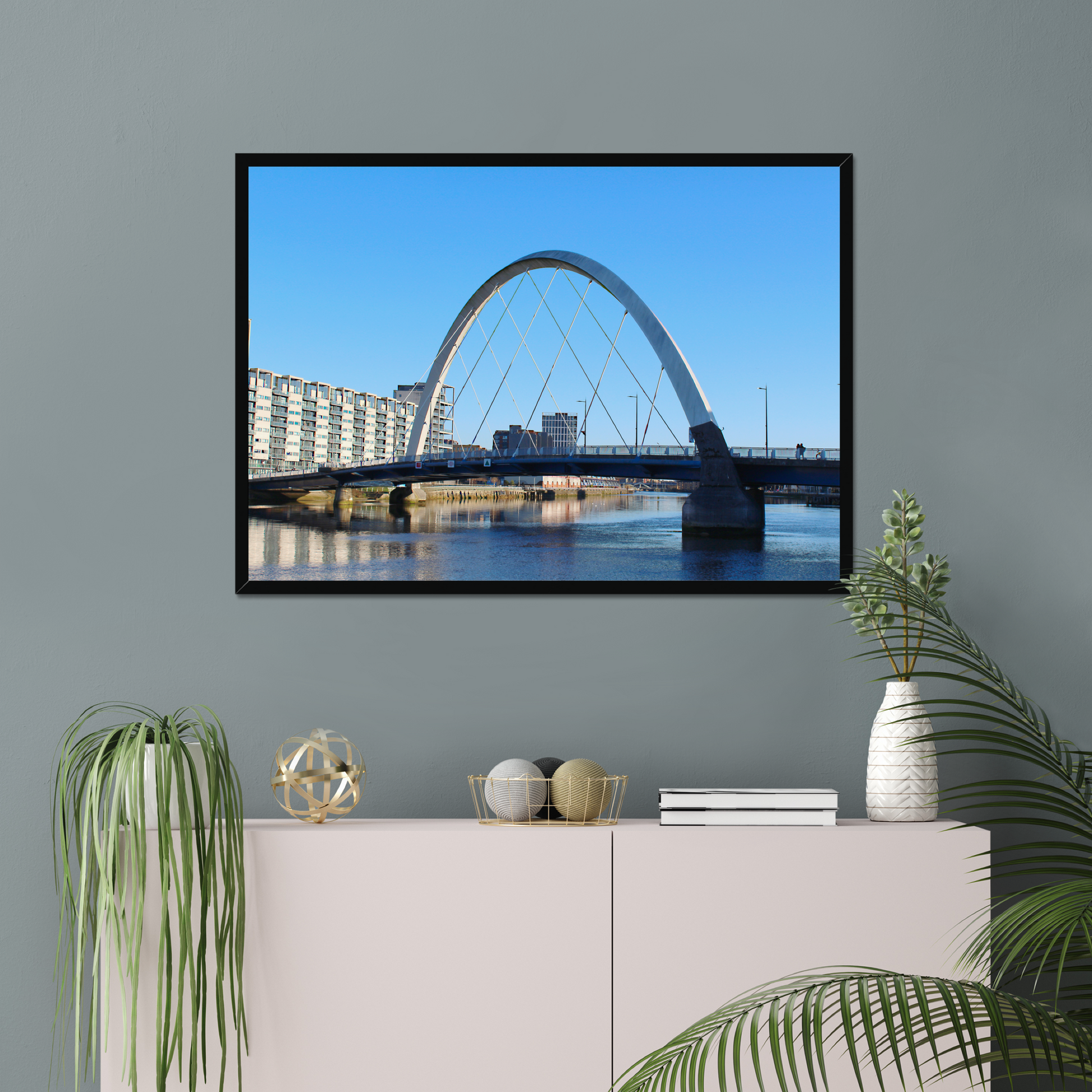 Framed photograph of a cityscape with a bridge on a wall above a white cabinet with decorative items.