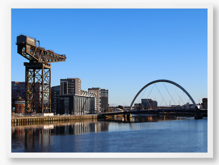 Framed Photo Of A Cityscape with a crane, buildings, and a bridge over water.