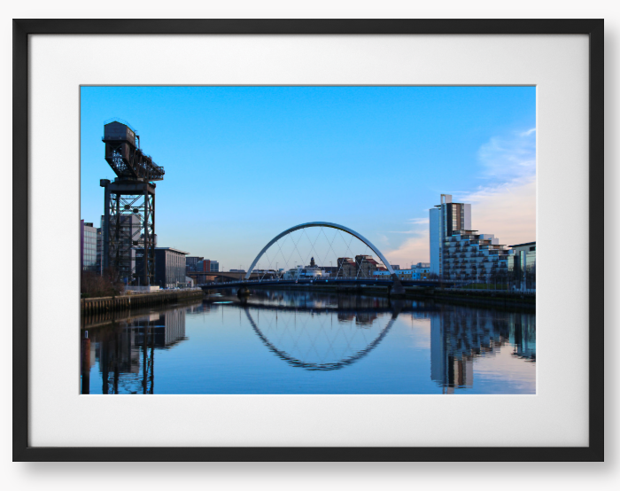A framed print featuring a photograph of Glasgow's River Clyde with reflections, including a prominent crane and modern cityscape in the background.