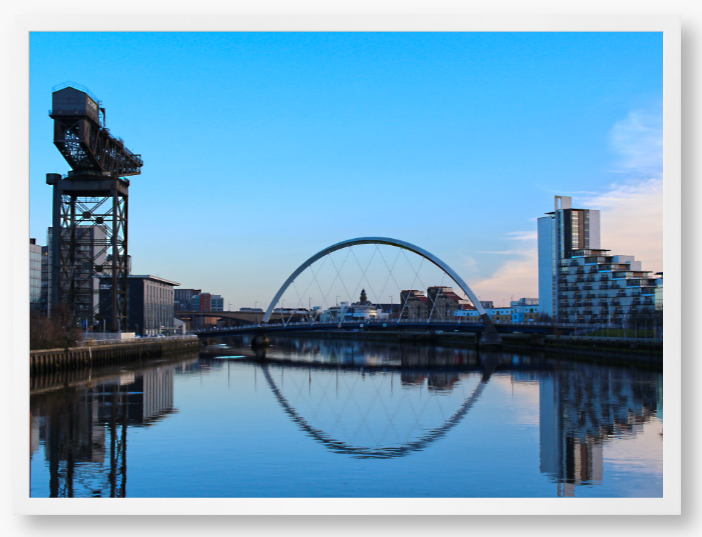 A framed print featuring a photograph of Glasgow's River Clyde with reflections, including a prominent crane and modern cityscape in the background.