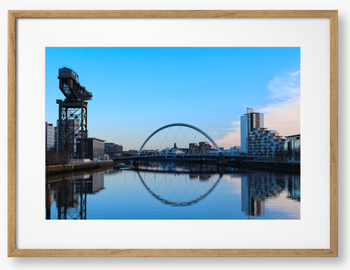 A framed print featuring a photograph of Glasgow's River Clyde with reflections, including a prominent crane and modern cityscape in the background.
