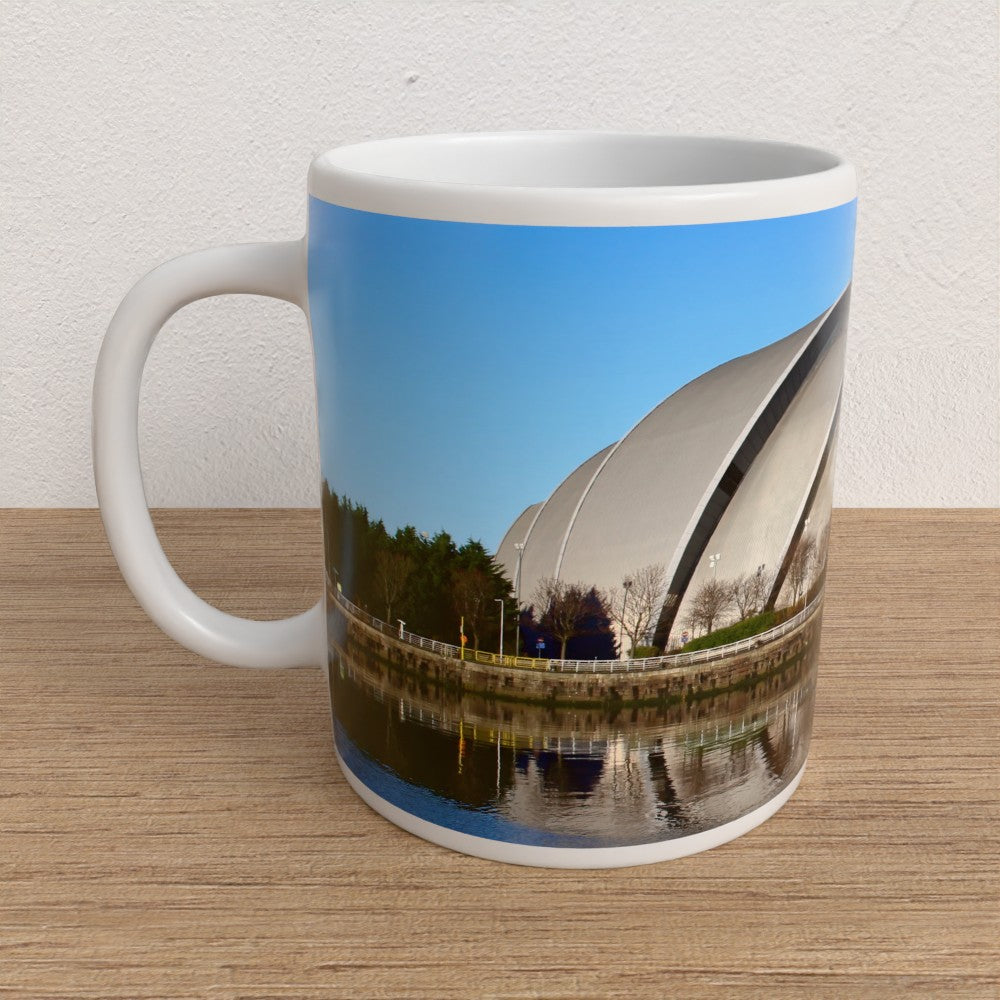 Mug with a scenic design of a building and trees on a wooden surface