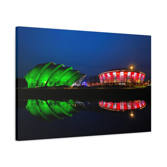 Two illuminated buildings, one green and one red and white, reflected in water at night.
