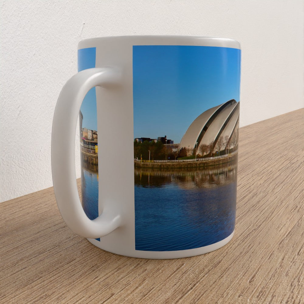 Mug with a scenic design of a lake and buildings on a wooden surface