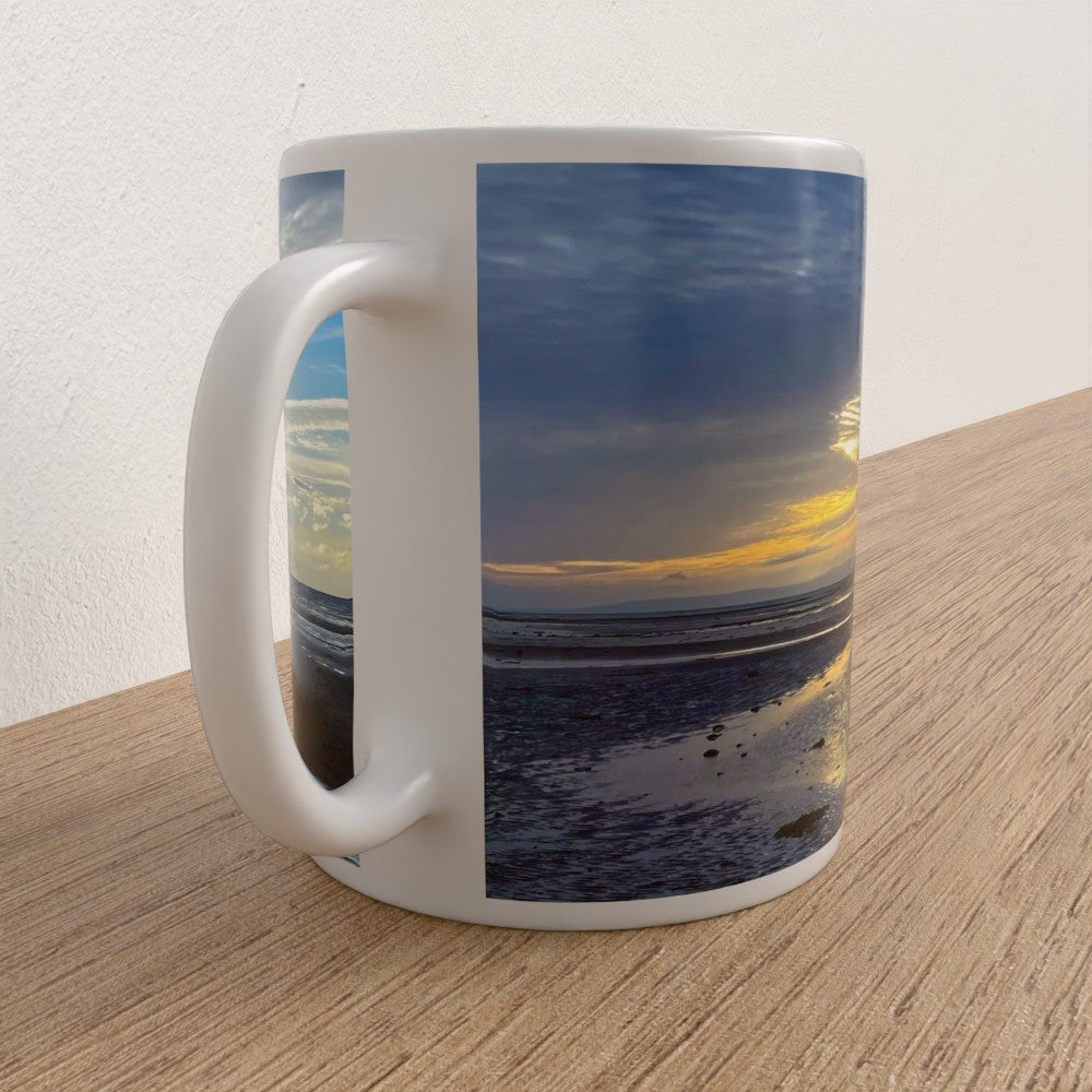White mug with a scenic design of a sunset over water on a wooden surface.
