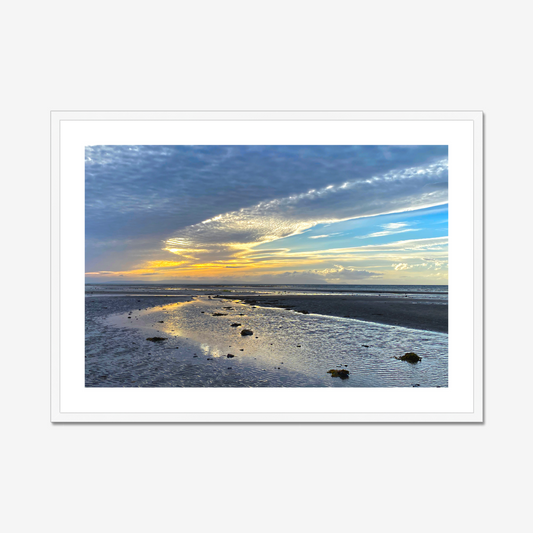 Framed photograph of a sunset over a beach with clouds and water reflections