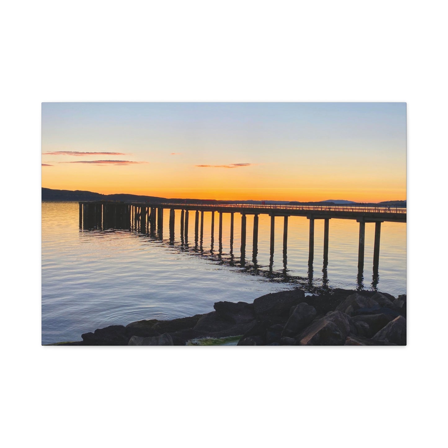 Sunset over a long pier with calm water reflecting the colors of the sky.