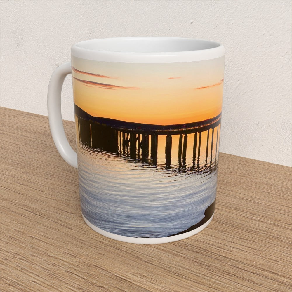 Mug with a sunset and pier design on a wooden surface