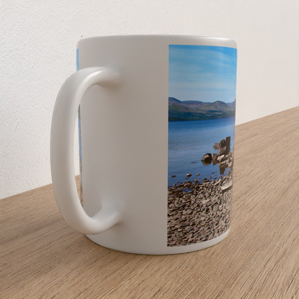 White mug with a scenic design of a lake and mountains on a wooden surface.