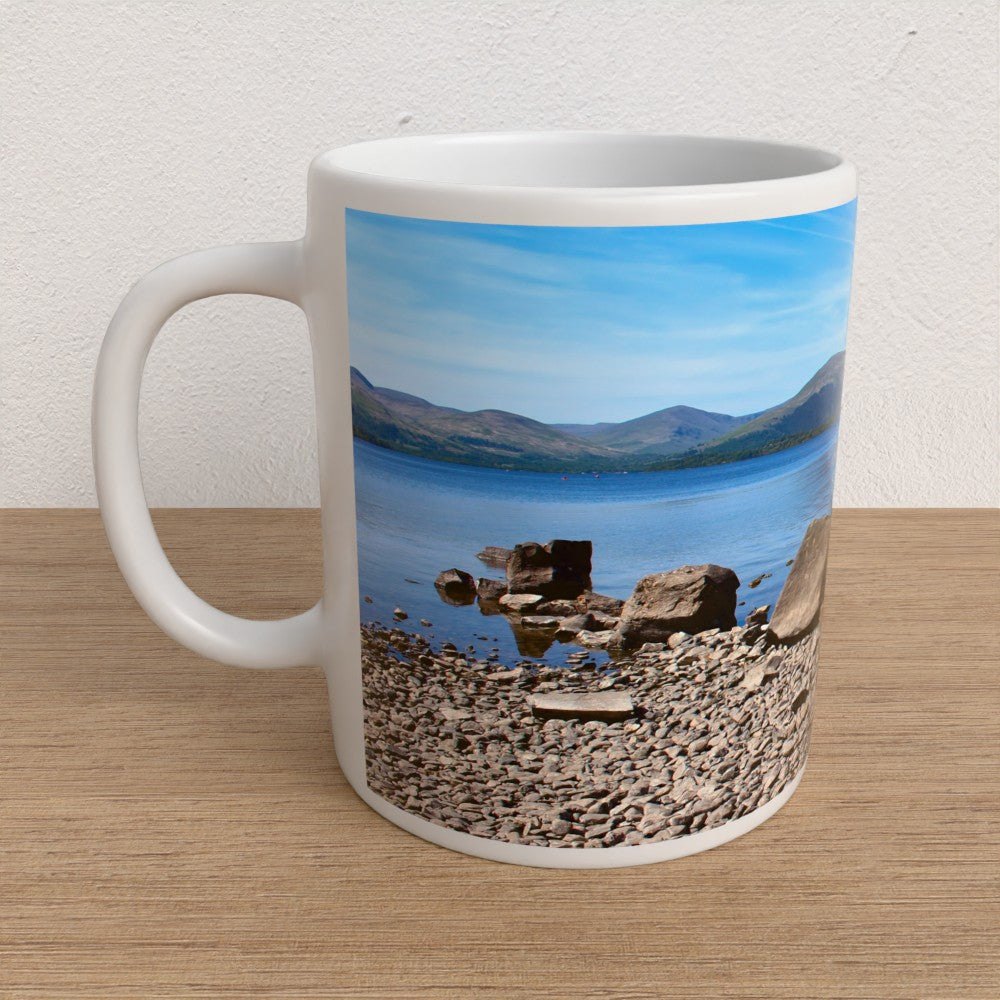 Mug with a scenic design of a lake and mountains on a wooden surface.