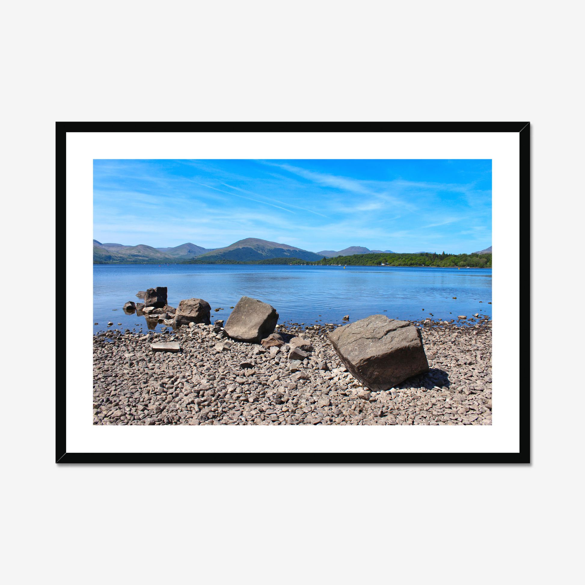 Framed photograph of a lake with mountains and rocks on a pebbly shore.