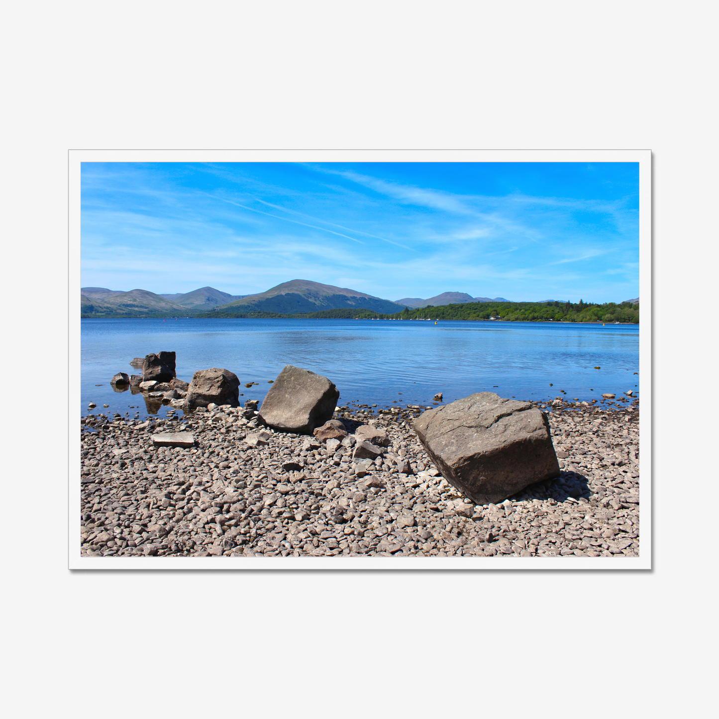 Framed photograph of a lake with mountains and rocks on a pebbly 
