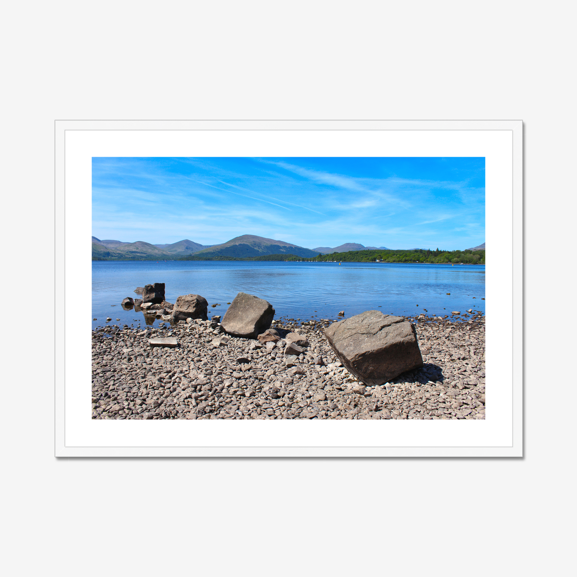 Framed photograph of a lake with mountains and rocks on a pebbly 