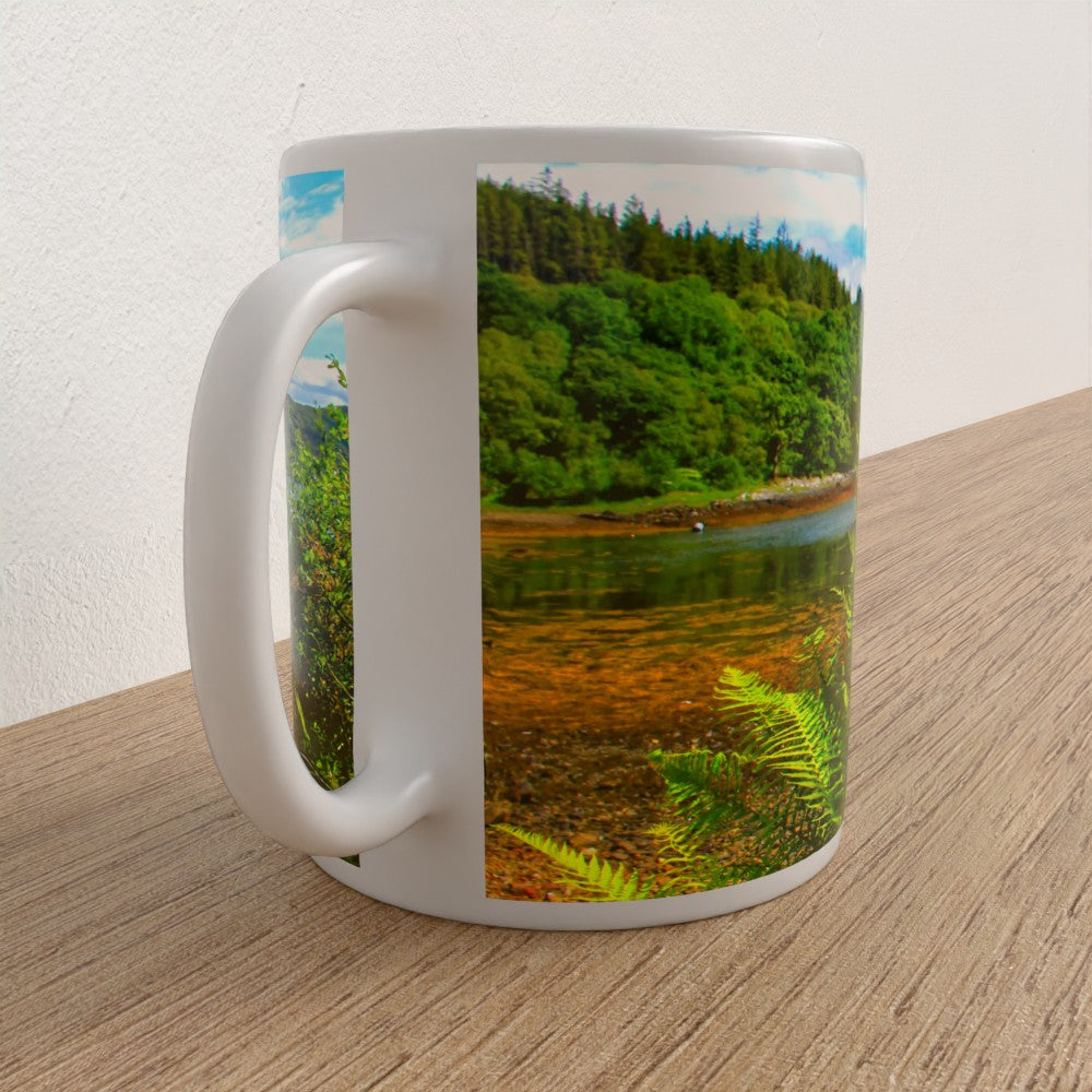 White mug with a scenic design of a lake and forest on a wooden surface.