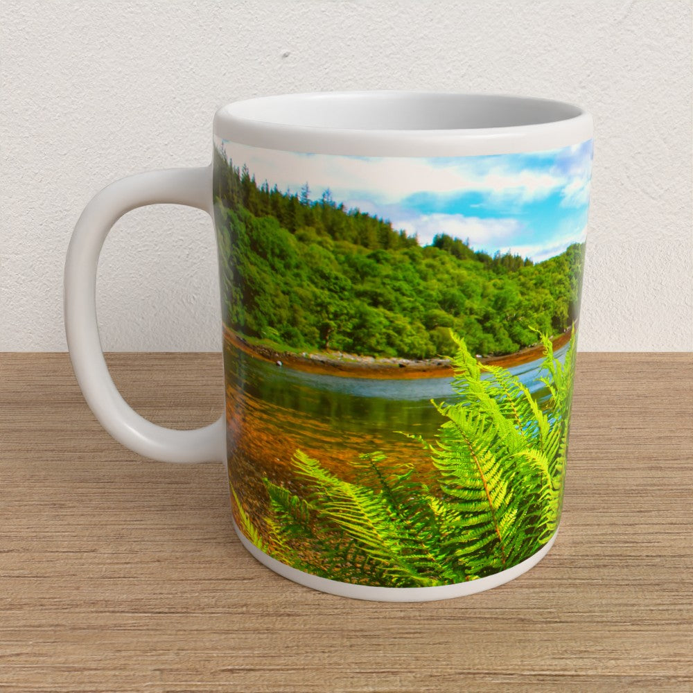 White mug with a scenic design of a lake and forest on a wooden surface.