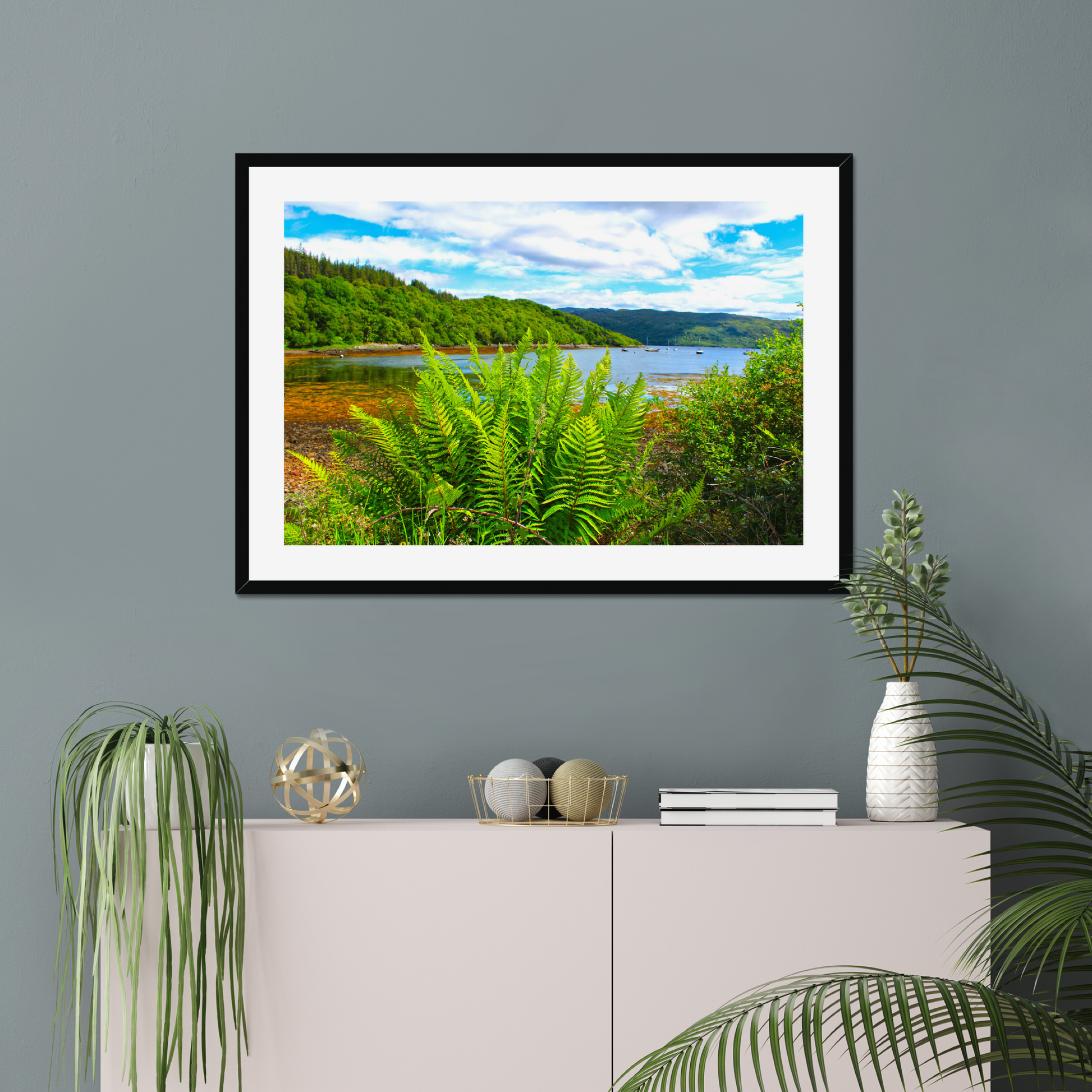 Framed photograph of a scenic landscape with a lake and forest, displayed on a wall above a cabinet.