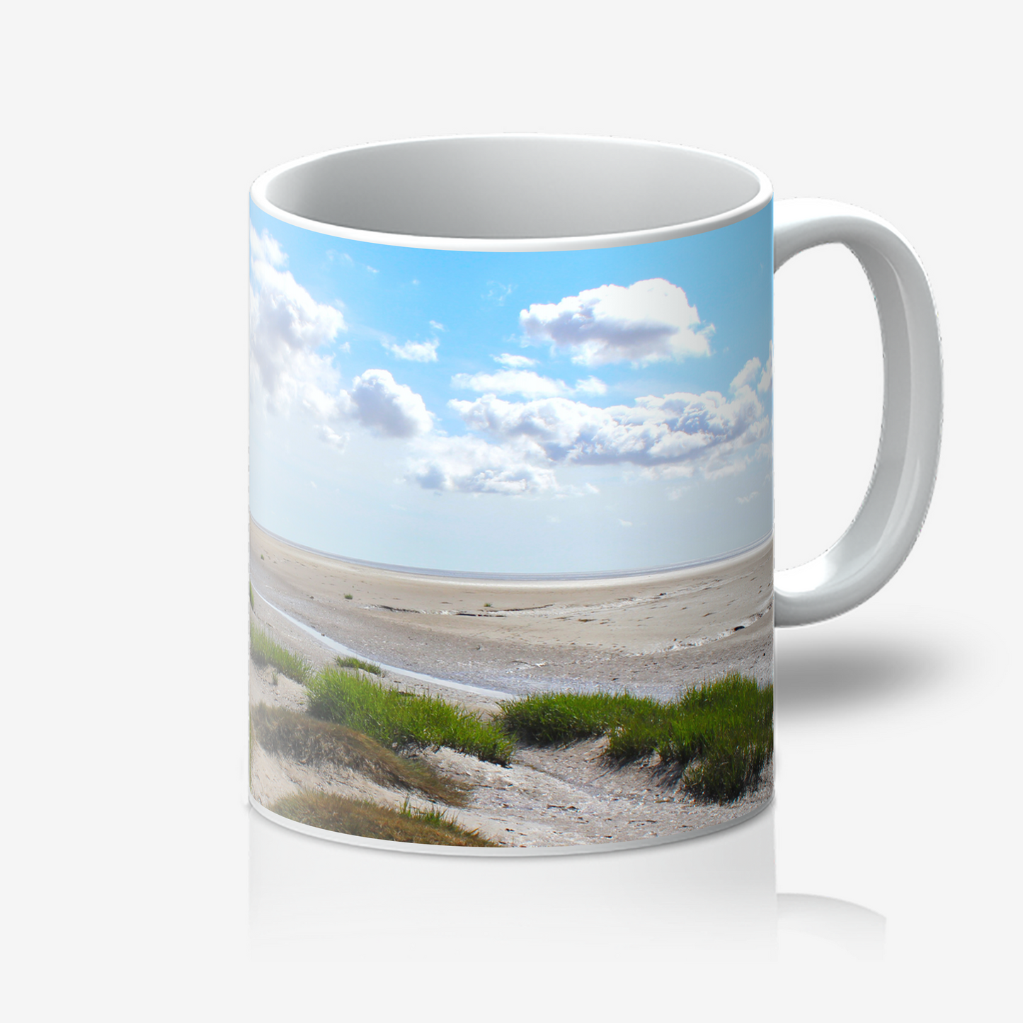 Mug with a beach scene featuring sand, grass, and clouds on a blue sky background.