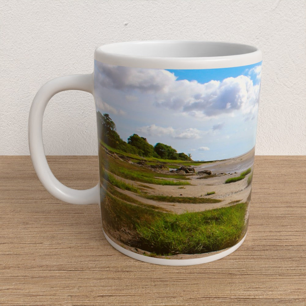 Mug with a scenic landscape of a beach and trees on a wooden table.