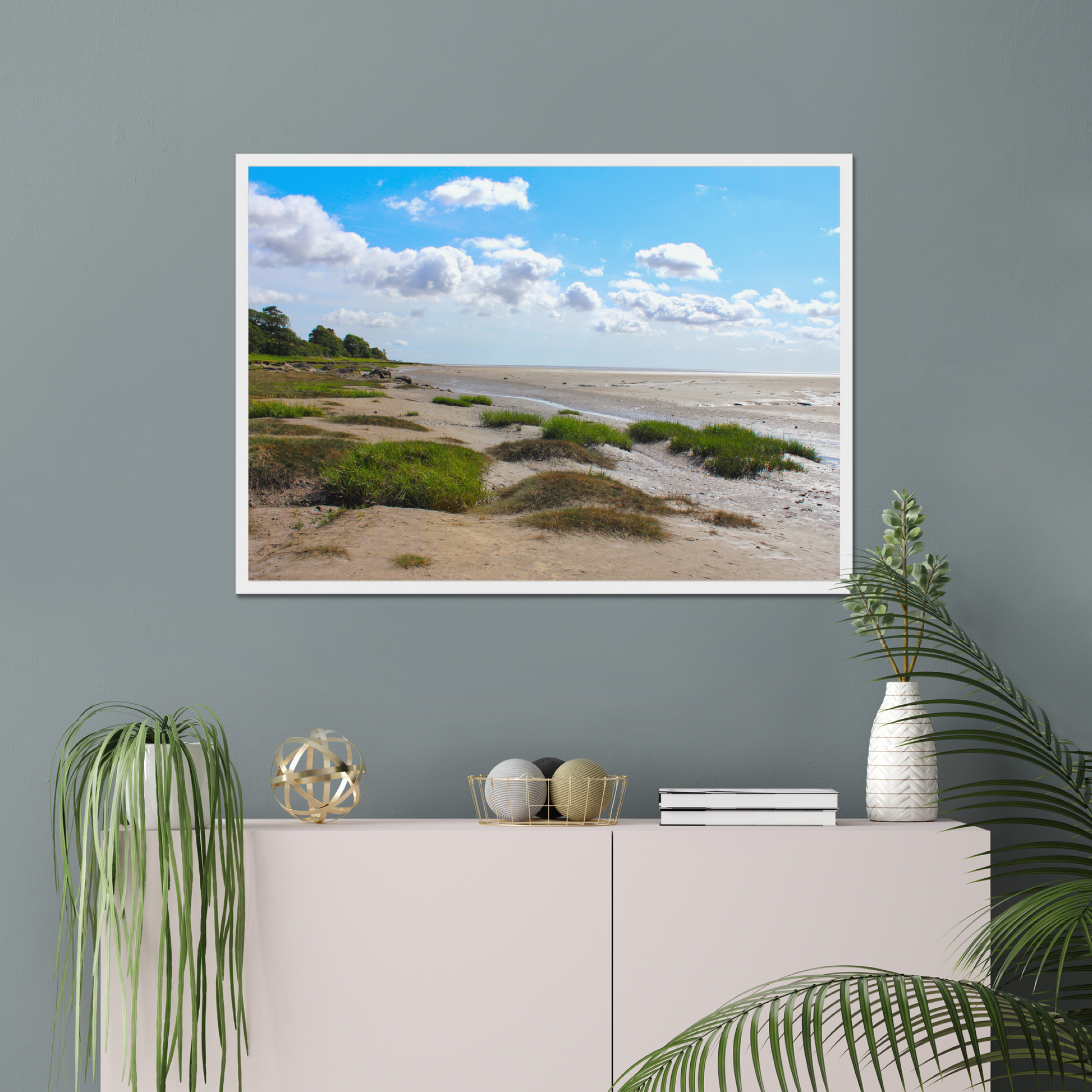 Framed landscape print of a beach scene on a gray wall above a white cabinet with decorative items.